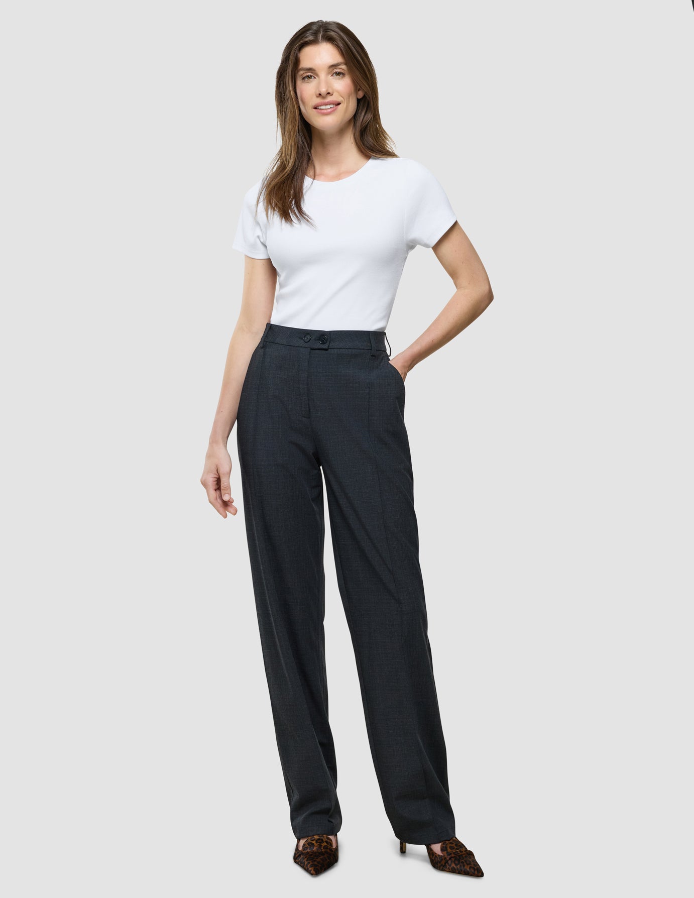 Eine lächelnde Frau präsentiert ein weißes T-Shirt, das in die „Women Nara Pants Straight Grey Flint“ gesteckt ist.